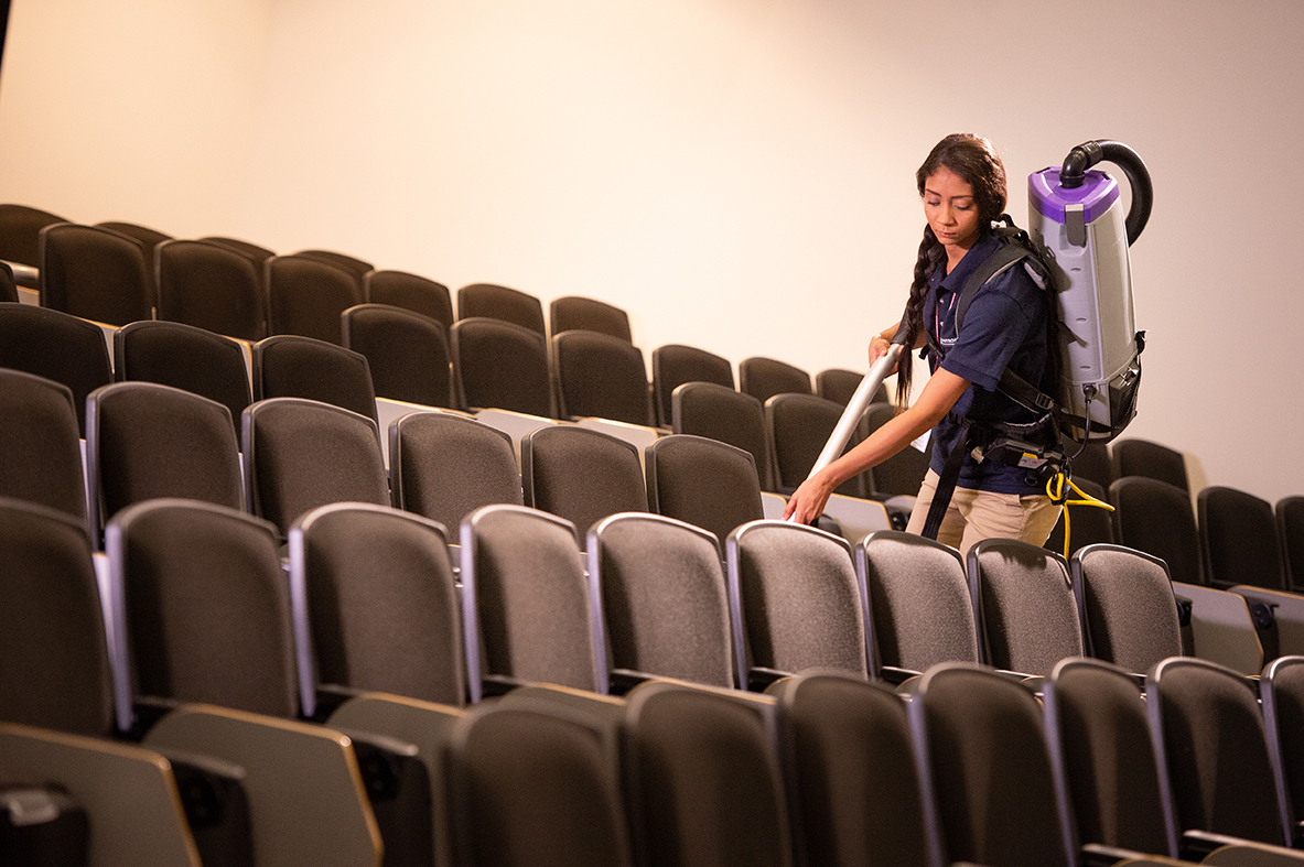 Janitronics technician using a backpack vacuum in a lecture hall