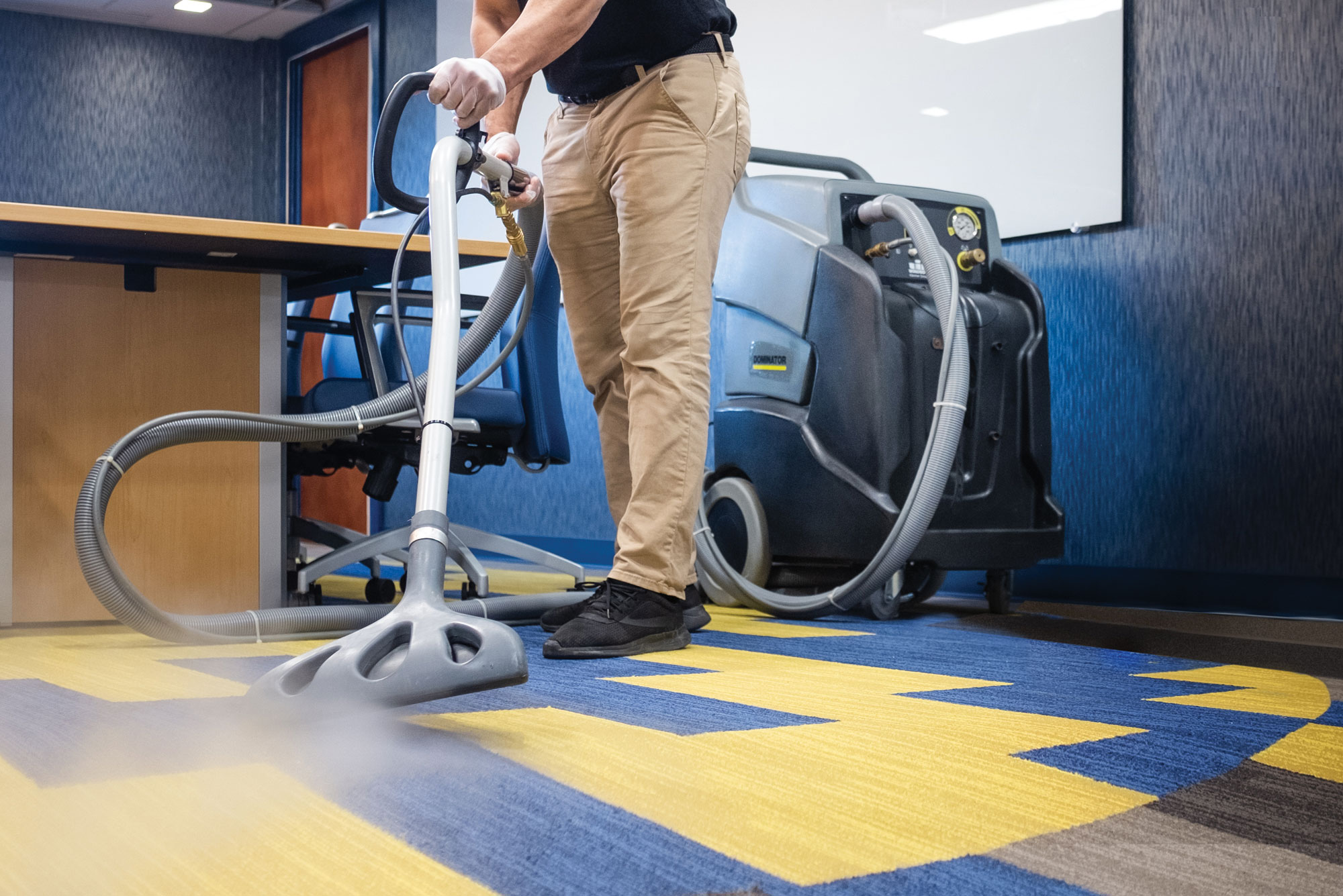 A person using a steam cleaner to clean a blue and yellow carpet.