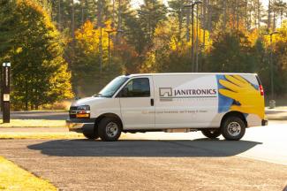 The sideways profile of the Janitronics van, with the logo facing the camera, parked in front of fall foliage