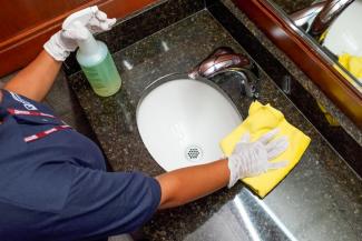 an overhead photo of a Janitronics custodian wiping the sink in a bathroom with cleaning solution and a microfiber cloth