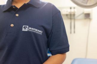 A close up of a Janitornics' team member's navy blue shirt, with the Janitronics logo embroidered in white