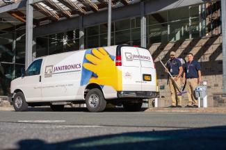 Two employees standing with Janitronics branded fleet van in front of a location