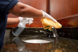 A Janitronics employee wiping a sink faucet with a yellow cloth.