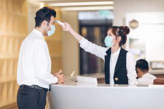 Reception area with masked employee scanning temperature of masked visitor.