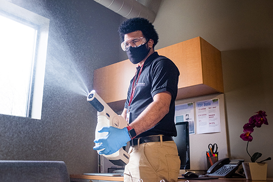 Janitronics cleaning technician using an electrostatic spray machine in an office