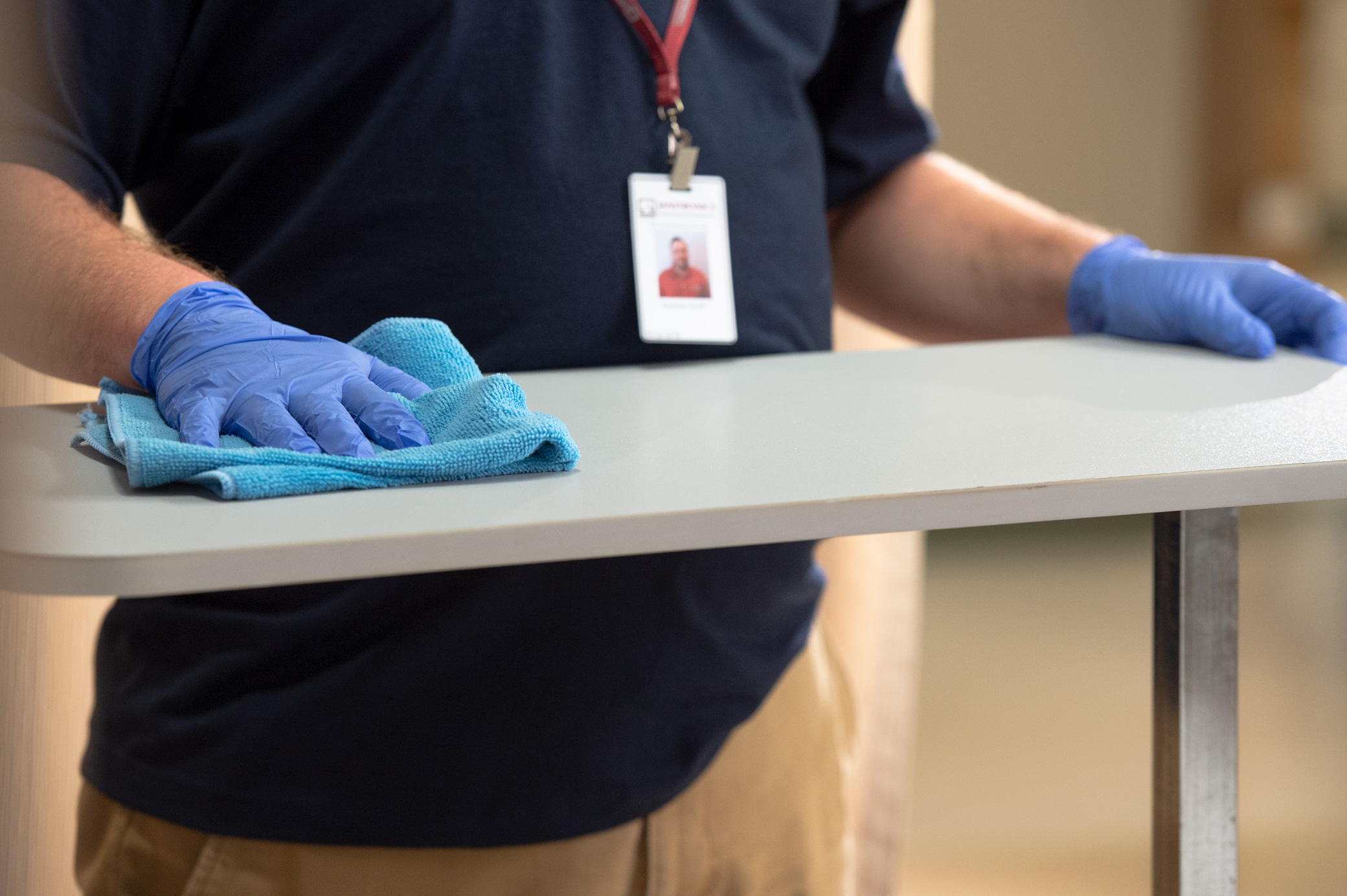 Close up of a Janitronics janitor cleaning a raised tabled with a blue microfiber cloth while wearing rubber gloves