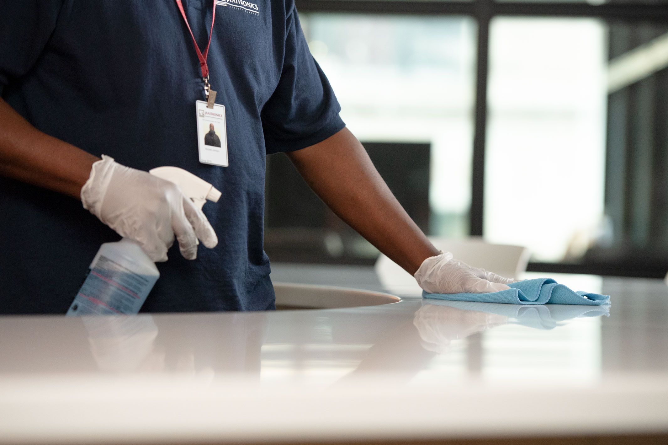 Employee cleaning office countertop with cleaning solution and blue cloth