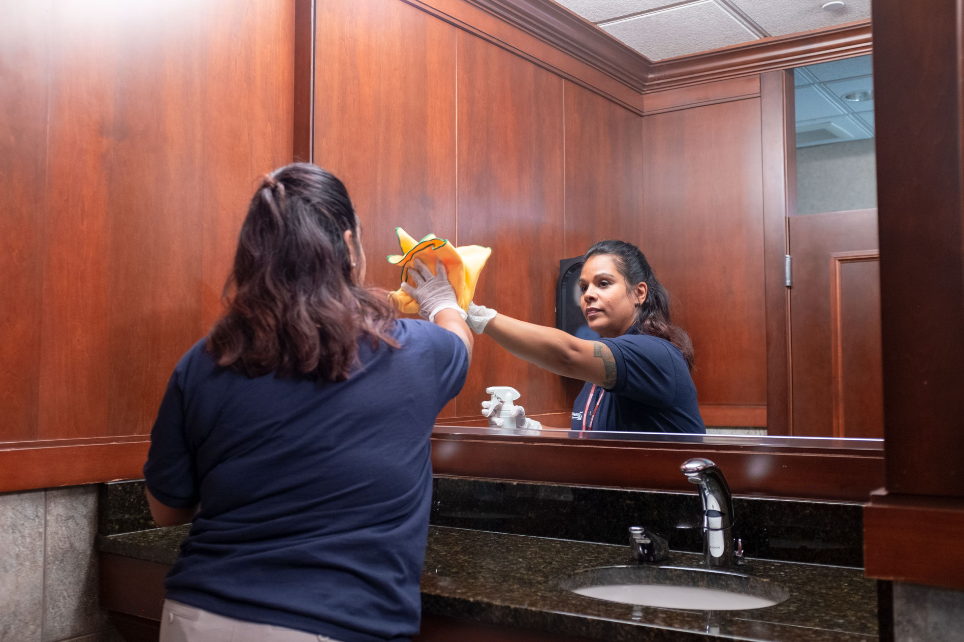 Janitronics employee cleaning bathroom mirror