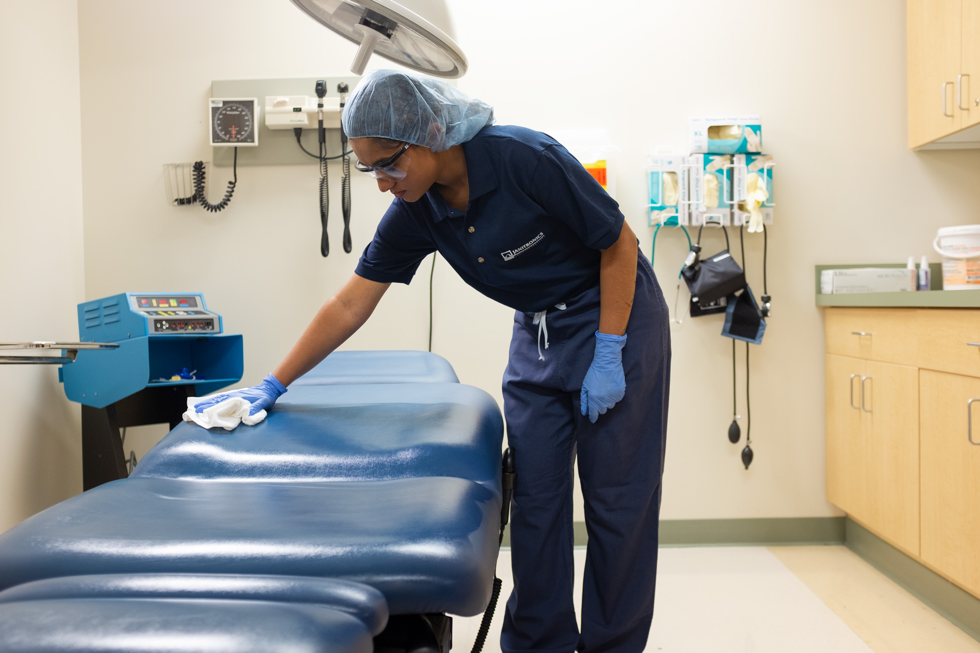 Employee cleaning a medical examination table wearing blue gloves